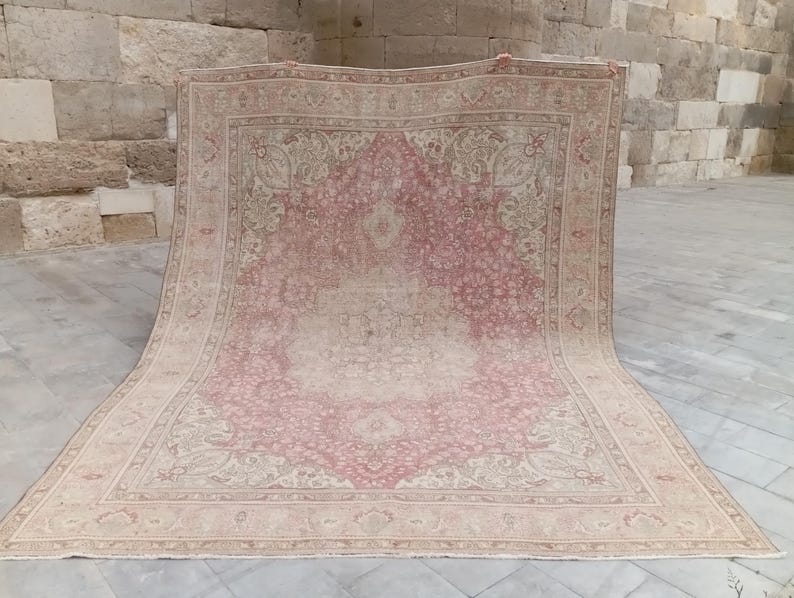 May include: A large rectangular area rug featuring a central medallion design in shades of dusty rose and cream. The rug displays an intricate floral pattern throughout the field and a wide decorative border with repeating motifs in muted tones.