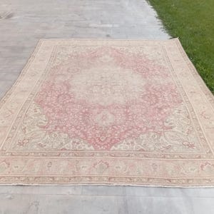 May include: A rectangular area rug featuring a central medallion design in shades of dusty rose and cream. The rug displays an intricate floral and vine pattern throughout the field, enclosed by a wide decorative border with repeating motifs.