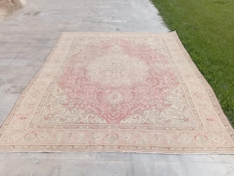 May include: A rectangular area rug featuring a central medallion design in shades of dusty rose and cream. The rug displays an intricate floral and vine pattern throughout the field, enclosed by a wide decorative border with repeating motifs.