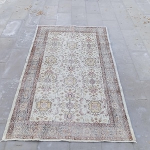 Puede incluir: Una alfombra vintage de color crema con un patrón floral y un borde marrón. La alfombra tiene un aspecto desgastado y descolorido, lo que le da un encanto rústico.