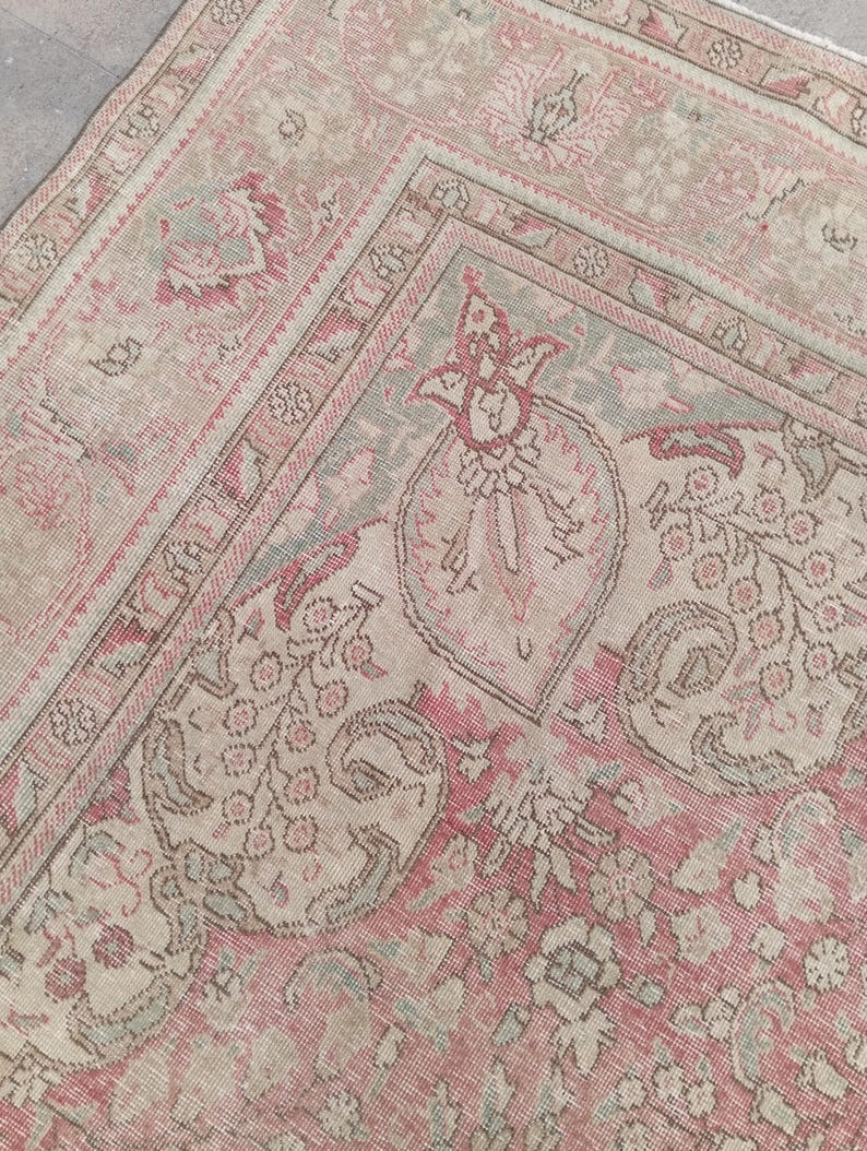 May include: A woven rug featuring a faded palette of dusty rose, muted sage green, and cream. The surface displays an intricate pattern of stylised floral motifs, paisley shapes, and geometric borders with a distressed, weathered texture.