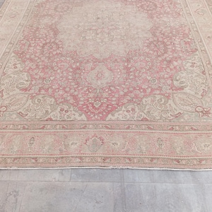 May include: A large rectangular area rug featuring a central medallion design in shades of dusty rose and beige. The rug displays an intricate floral pattern throughout the field and a wide decorative border with repeating botanical motifs.