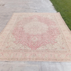 May include: A rectangular area rug featuring a central medallion design in shades of dusty pink and cream. The rug displays an intricate floral and vine pattern throughout the field, enclosed by a wide decorative border with repeating motifs.