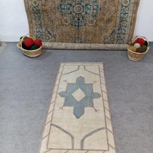 May include: A light blue and beige vintage rug with a geometric pattern. The rug has a diamond shape in the centre and a border with a striped design.