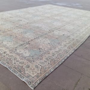 May include: Large rectangular area rug with a faded, vintage appearance. The rug features a central field with muted pastel colors, including beige, blue, and pink. A detailed border frames the design, adding a touch of elegance to the floor covering.