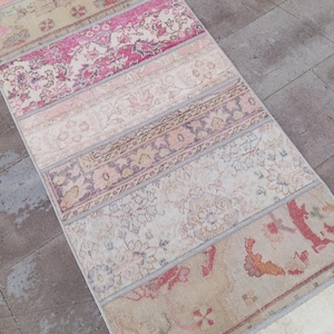 May include: A patchwork rug with a mix of floral and geometric designs in pink, beige, and brown. The rug is made from several rectangular strips sewn together. The rug's design creates a unique and textured surface.
