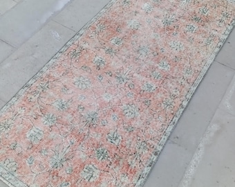 Puede incluir: Una alfombra vintage de color rosa y verde con estampado floral y aspecto descolorido. La alfombra tiene forma rectangular y está hecha de material tejido.