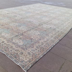May include: Large, rectangular area rug with a faded, vintage appearance. The rug features a central field with a repeating pattern in muted tones of beige, blue, and rose. A detailed border frames the design, adding a touch of elegance to the floor covering.