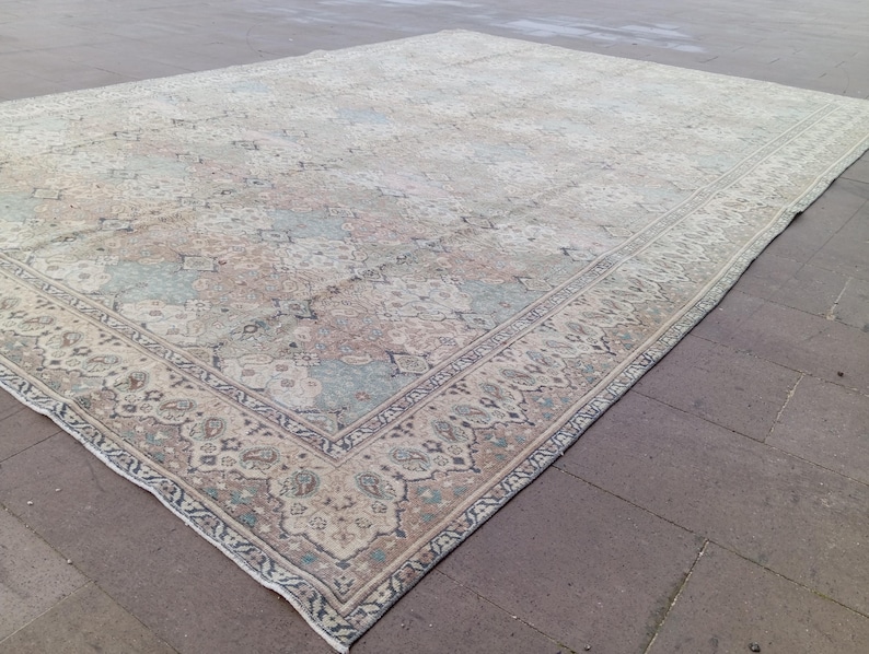 May include: Large, rectangular area rug with a faded, vintage appearance. The rug features a central field with a repeating pattern in muted tones of beige, blue, and rose. A detailed border frames the design, adding a touch of elegance to the floor covering.