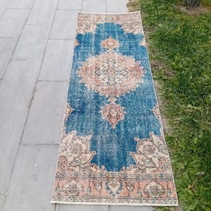 May include: A rectangular, vintage-style rug with a distressed appearance. The rug features a central medallion design in shades of peach and cream against a blue background. The border is a mix of peach, cream, and blue, creating a classic, aged aesthetic.