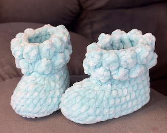 May include: A pair of light blue knitted baby booties with a fluffy texture. The booties have a folded cuff and a rounded toe.