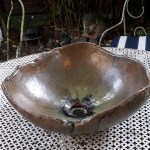May include: A large, brown ceramic bowl with a unique, irregular shape and a glazed finish. The bowl has a dark brown rim and a slightly green hue in the center.