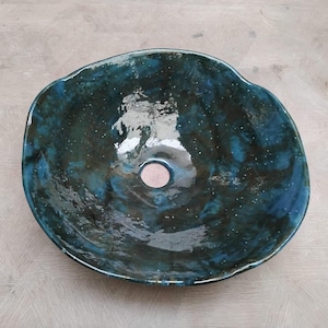 May include: A large, round, ceramic sink with a dark blue and green glaze. The sink has a small, round drain hole in the center.