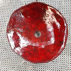 May include: A red ceramic sink with a round shape and a drain hole in the center. The sink has a glossy finish and a textured surface.