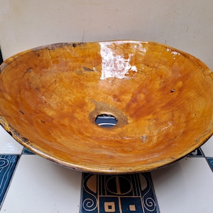 May include: A round, bowl-shaped vessel sink crafted from natural wood with a polished, glossy finish. The surface displays a warm, golden-brown grain with visible knots and organic textures, featuring a centered circular drain opening.