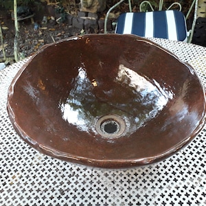 May include: A brown ceramic sink with a drain hole in the center. The sink is sitting on a white metal table with a crosshatch pattern.