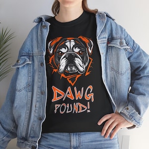 Puede incluir: Camiseta negra con un gráfico de la cara de un bulldog en naranja y blanco. El texto "DAWG FOUND!" está impreso en naranja debajo del bulldog.