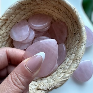 May include: A woven basket filled with rose quartz heart-shaped stones. The stones are a light pink color and are smooth and polished.