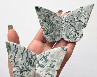 May include: Two green and white agate butterfly shaped crystal carvings. The butterflies are polished and have a natural, marbled pattern.