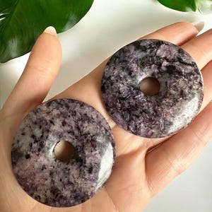 May include: Two purple and gray gemstone donut shaped pendants with a hole in the center.
