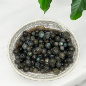 May include: A white bowl filled with iridescent black and green labradorite gemstone beads.