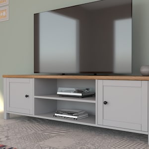 May include: A gray TV stand with a light wood top and two cabinet doors. The stand has open shelves with a record player and books. A large flat-screen TV sits on top. A small gray decorative sphere is on the right side.