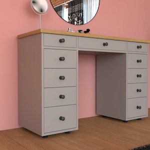 Puede incluir: Una cómoda gris con una tapa de madera y ocho cajones. La cómoda tiene pomos negros en cada cajón. La cómoda está frente a una pared rosa.