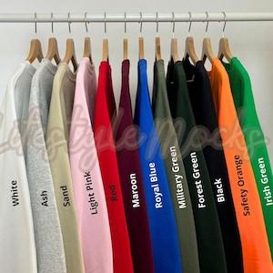 Puede incluir: Un estante con 12 sudaderas de diferentes colores, incluyendo blanco, ceniza, arena, rosa claro, rojo, granate, azul real, verde militar, verde bosque, negro, naranja de seguridad y verde irlandés.