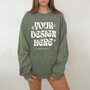 Op de afbeelding: Een groen sweatshirt met de tekst "YOUR DESIGN HERE" in wit. De tekst is in een retro-lettertype met sterren aan beide kanten. De tekst "Lifestyle Mocks Co." is in een kleiner lettertype onder de hoofdtekst gedrukt.