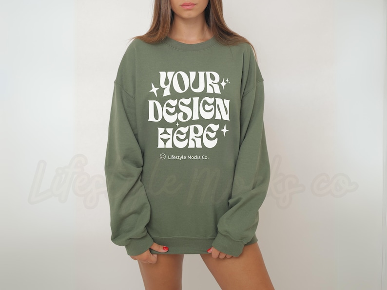 Op de afbeelding: Een groen sweatshirt met de tekst "YOUR DESIGN HERE" in wit. De tekst is in een retro-lettertype met sterren aan beide kanten. De tekst "Lifestyle Mocks Co." is in een kleiner lettertype onder de hoofdtekst gedrukt.