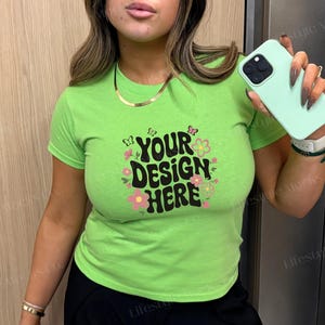 Puede incluir: Una camiseta verde lima con mangas cortas y cuello redondo. La camiseta tiene un estampado gráfico de flores y mariposas con el texto "YOUR DESIGN HERE" en negro.