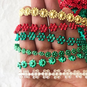 Pode incluir: Cinco fios de guarnição decorativa com contas em forma de flor. A guarnição é de várias cores, incluindo dourado, vermelho, verde e branco.
