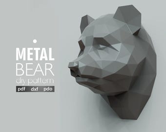 May include: A gray, geometric metal bear head mounted on a wall. The image includes the text "METAL BEAR diy pattern" with file type options: pdf, dxf, and pdo. The logo for artaxis studio is in the bottom right corner.