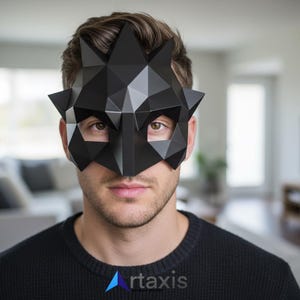 Op de afbeelding: Een zwart geometrisch masker met een puntig kroontjesontwerp. Het masker heeft hoekige facetten en bedekt de ogen en neus. Het masker wordt gedragen door een persoon die een zwarte trui draagt. Het logo voor "rtaxis" staat in de onderste hoek.