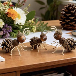 Puede incluir: Tres figuras de hormigas hechas a mano con piñas, bellotas y alambre, con ojos saltones. Las hormigas están dispuestas sobre una superficie de madera, con un ramo de flores al fondo. También hay una gran piña.