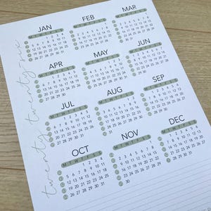 Op de afbeelding: Een witte papieren kalender voor het jaar twintig twintig, waarbij elke maand in een rasterformaat wordt weergegeven. De dagen van de week zijn afgekort en de data staan in een eenvoudig, leesbaar lettertype. De kalender heeft een minimalistisch ontwerp.