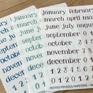 May include: Three sheets of clear sticker paper with month names and numbers printed in blue, green, and purple. The sheets are labeled "PETITES PENSÉES PAPETERIE - Watercolor Month"