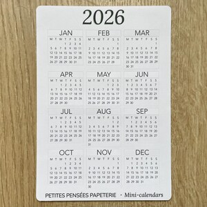 May include: A white mini-calendar card for the year 2026, featuring a monthly calendar layout with the days of the week and dates. The text "2026" is at the top, with "PETITES PENSEES PAPETERIE Mini-calendars" at the bottom.