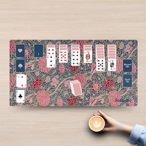 May include: A rectangular play mat featuring a dark blue background with a dense floral pattern of pink and red blossoms. The mat displays a digital solitaire game layout with various playing cards, a discard pile, a stock pile, and the word Solitaire.