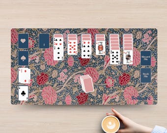 May include: A rectangular play mat featuring a dark blue background with a dense floral pattern of pink and red blossoms. The mat displays a digital solitaire game layout with various playing cards, a discard pile, a stock pile, and the word Solitaire.