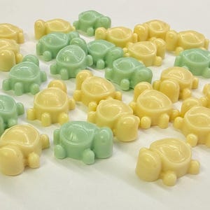 May include: A collection of small, moulded turtle-shaped figures in pale yellow and soft mint green colours. Each figure features a smooth, rounded shell and four distinct legs, arranged in a scattered group on a plain, neutral white surface.