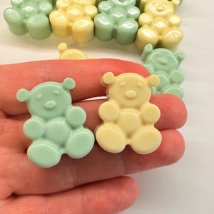 Könnte beinhalten: Eine Sammlung kleiner, glatter, bärenförmiger Figuren in Pastellgrün und Hellgelb. Die Bärenfiguren haben abgerundete Ohren, eine kreisförmige Schnauze und definierte Gliedmaßen. Mehrere Bärenfiguren sind in einer Gruppe angeordnet.