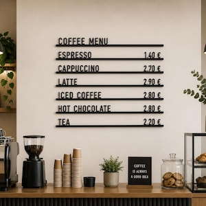 May include: A wall-mounted black menu board with horizontal rails displaying the text COFFEE MENU, ESPRESSO 1.40 €, CAPPUCCINO 2.70 €, LATTE 2.90 €, ICED COFFEE 2.80 €, HOT CHOCOLATE 2.80 €, and TEA 2.20 € in a clean, sans-serif font style.