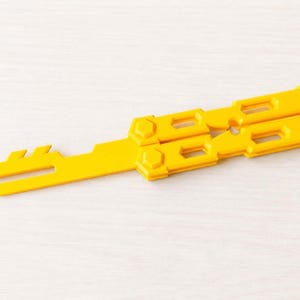 Op de afbeelding: Een felgele multitool met een mes en een handvat met rechthoekige uitsparingen. De tool is gemaakt van plastic en is ontworpen om dubbel te vouwen. De tool is ongeveer 15 cm lang.