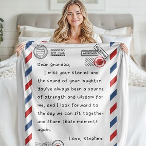 May include: A white blanket with a red, white, and blue design that looks like an envelope. The blanket has a handwritten message that says "Dear grandpa, I miss your stories and the sound of your laughter. You've always been a source of strength and wisdom for me, and I look forward to the day we can sit together and share those moments again. Love, Stephen."