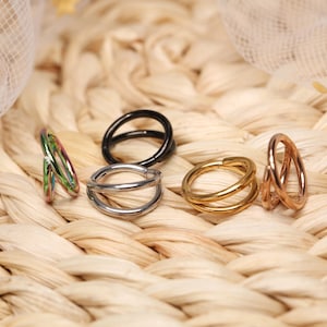 Op de afbeelding: Vijf verschillende gekleurde dubbele oorringen. De hoepels zijn gemaakt van metaal en zijn verkrijgbaar in zwart, zilver, goud, rosé goud en iriserend groen.