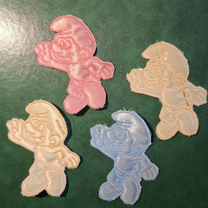 May include: Four embroidered Smurf patches in pink, light yellow, and light blue. Each patch features a Smurf character in a dynamic pose, with detailed facial features and clothing. The patches are on a green background.