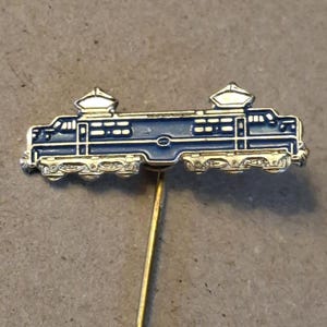 以下が含まれることがあります： 金色のピンバックが付いた、青と銀色の列車のピン。ピンは、銀色のアクセントが付いた列車のエンジンの詳細なデザインが特徴です。列車のピンは収集品です。