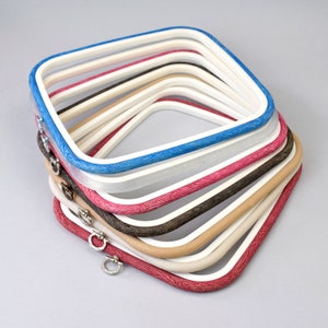 Op de afbeelding: Een set van acht borduurringen in verschillende maten en kleuren, waaronder blauw, wit, roze, bruin en beige. De ringen zijn op elkaar gestapeld en hebben een houtnerfpatroon.