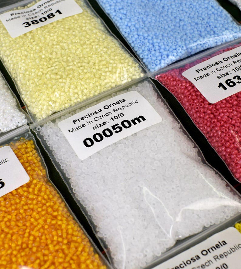 May include: Close-up of six bags of small, round beads. The bags are labeled with the brand name "Preciosa Ornela" and the size of the beads. The beads are in various colors, including yellow, white, light blue, and pink.
